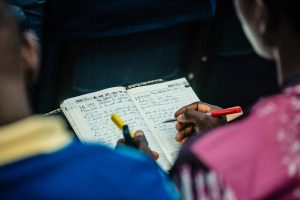 Người chơi theo dõi trận bóng và ghi chép kế hoạch chia vốn vào sổ tay